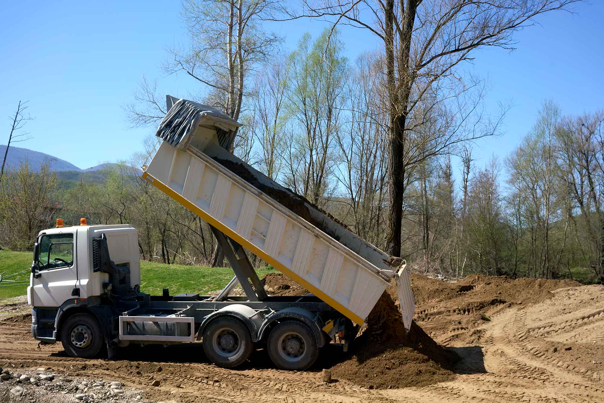 White dump truck unloading soil at a construction site.